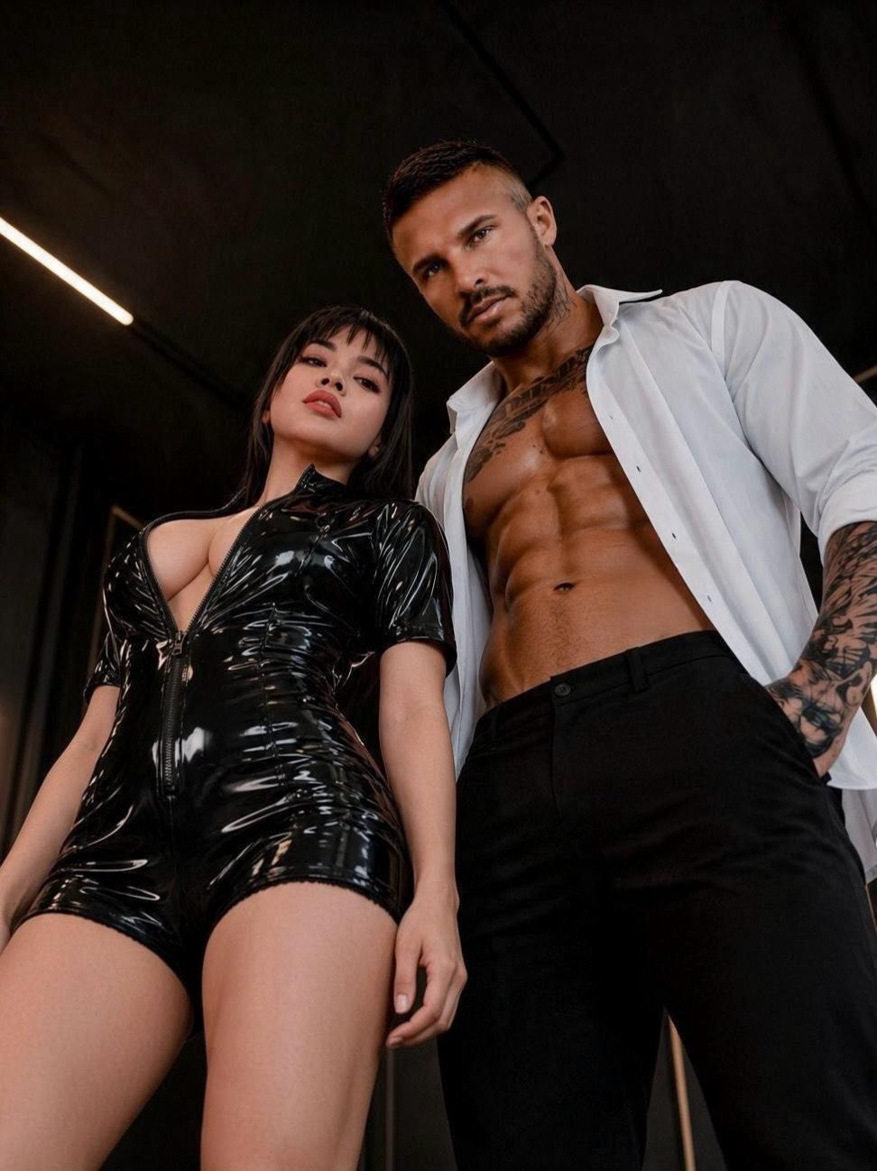 The couple photographed from a low angle in black latex and an open white shirt
